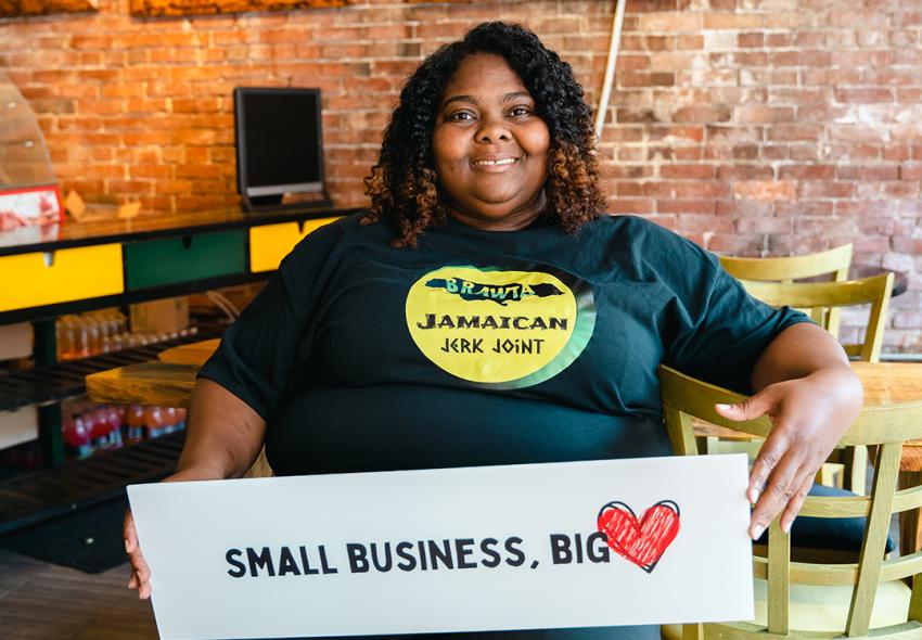 Christine Allen, owner of Brawta Jamaican Jerk Joint, holding a sign "Small Business, Big Heart"