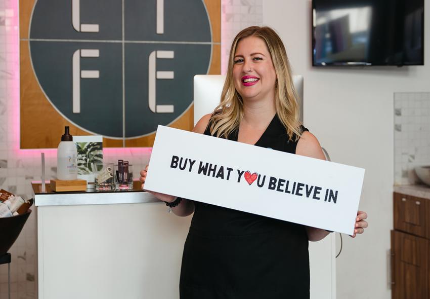 Virginia Wilbur, manager of Life SalonSpa, holding a sign "Buy What You Believe In"