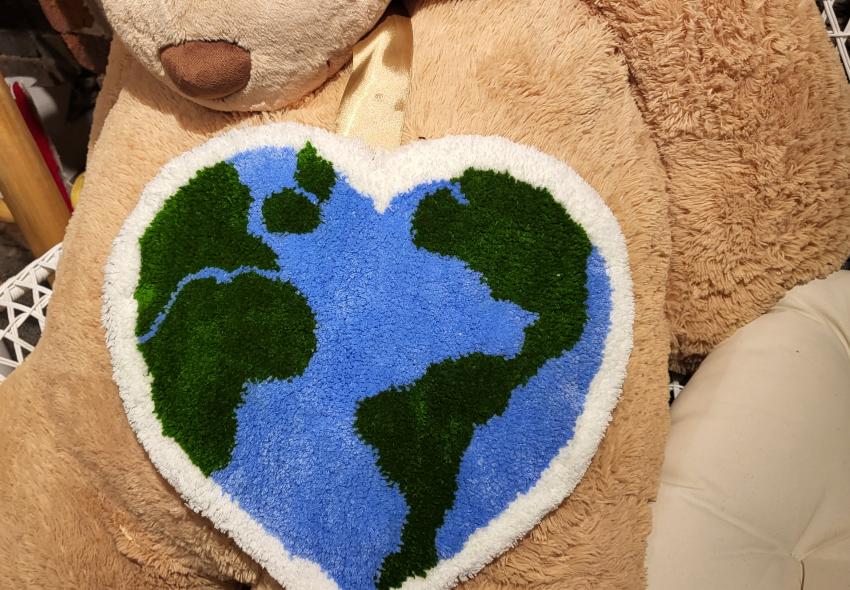 A tufting art piece of a heart with a map/globe design on a teddy bear
