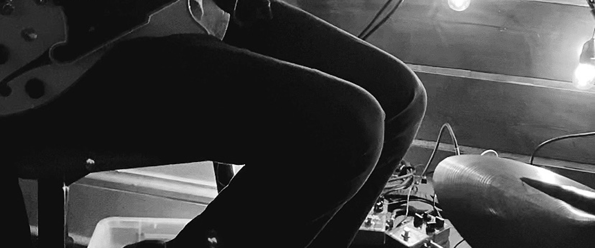 Black and white image of Gabe Mink on a stool, playing guitar and singing.