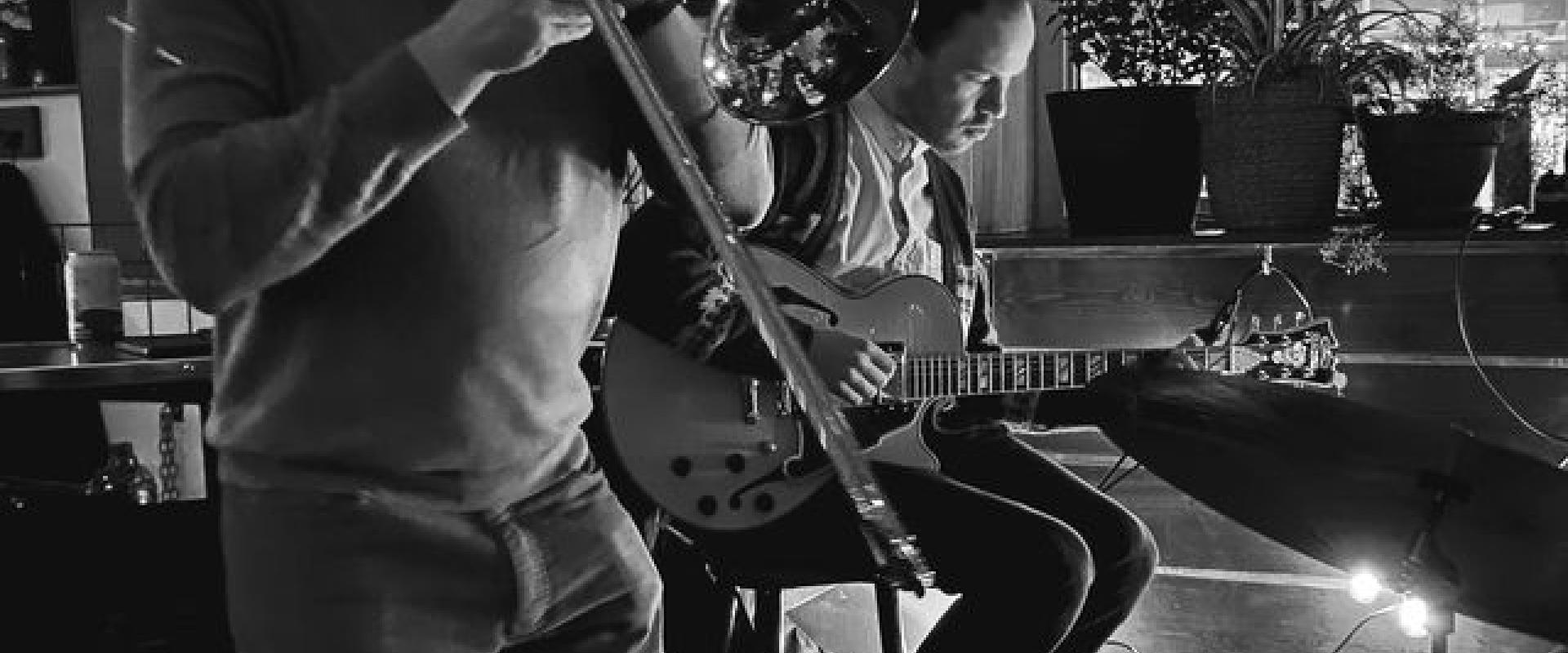 Musician playing the trombone and Gabe Mink playing guitar in the background. 