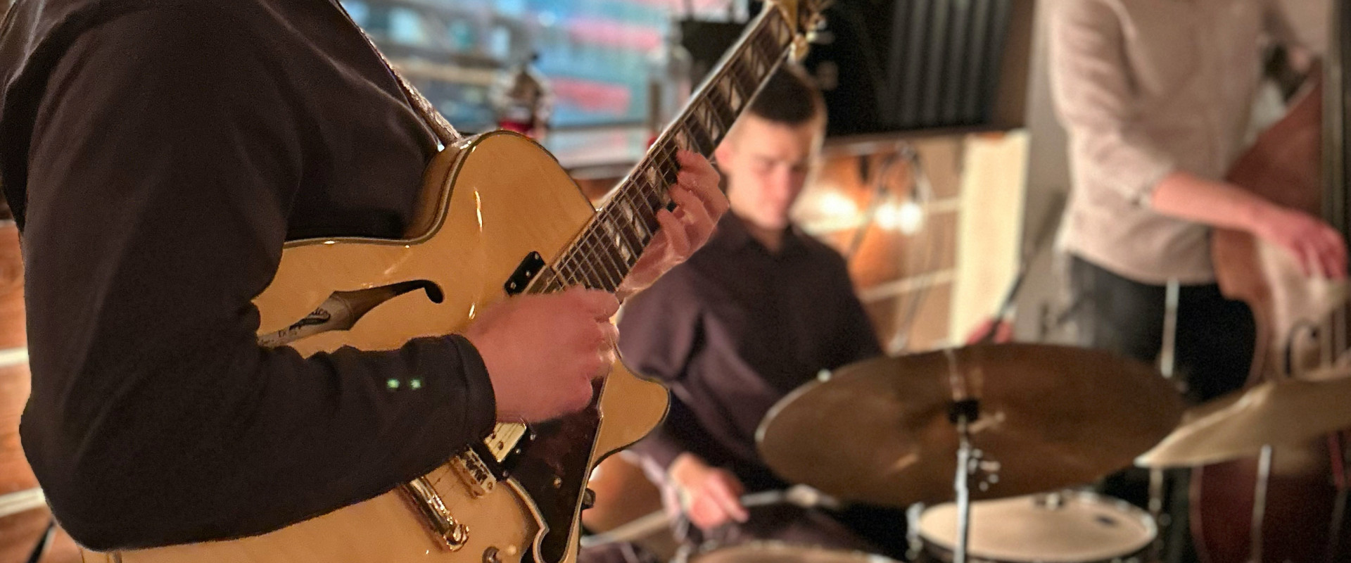 Gabe Mink playing guitar with a drummer and a standup bassist in the background.