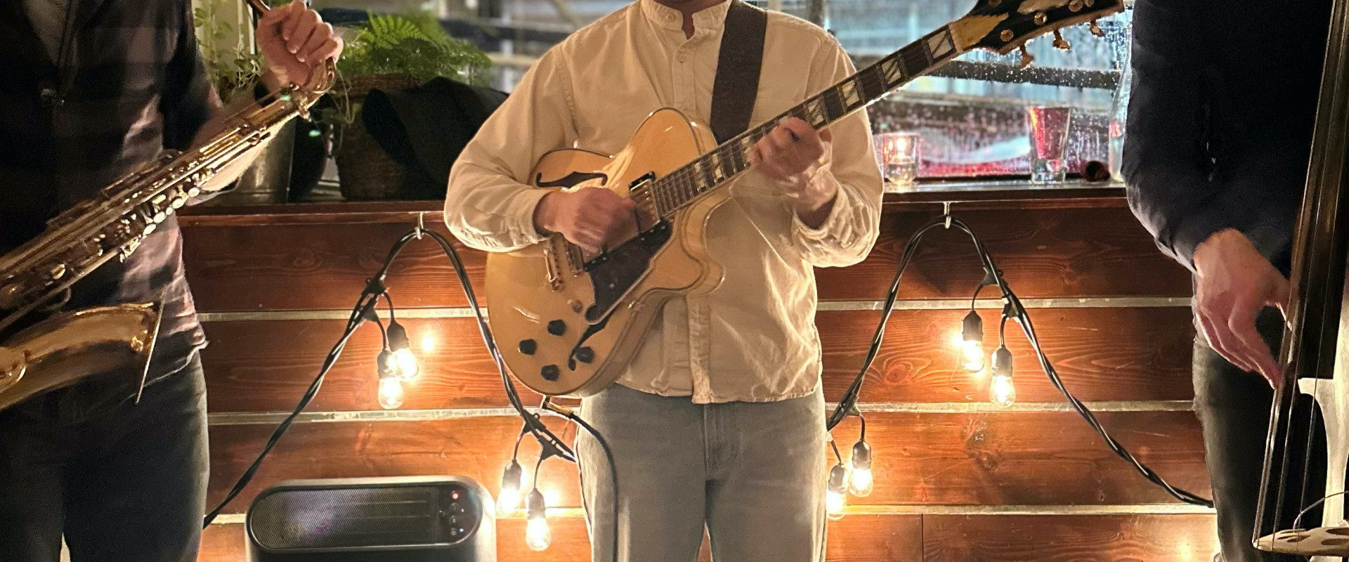 Gabe Mink playing guitar in the middle of a saxophonist and a standup bassist.