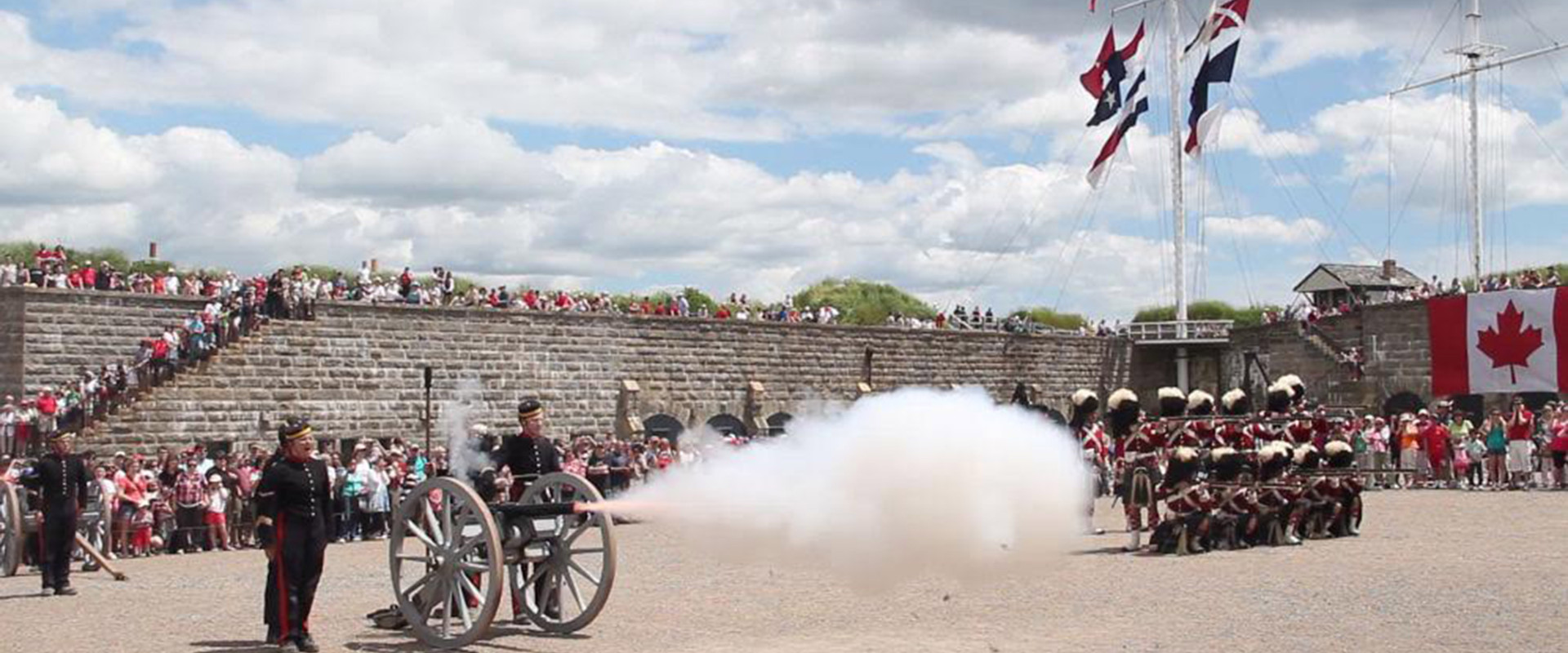 Historic military display including cannon firing on the Parade Square. Military flags flying on mast in background. 