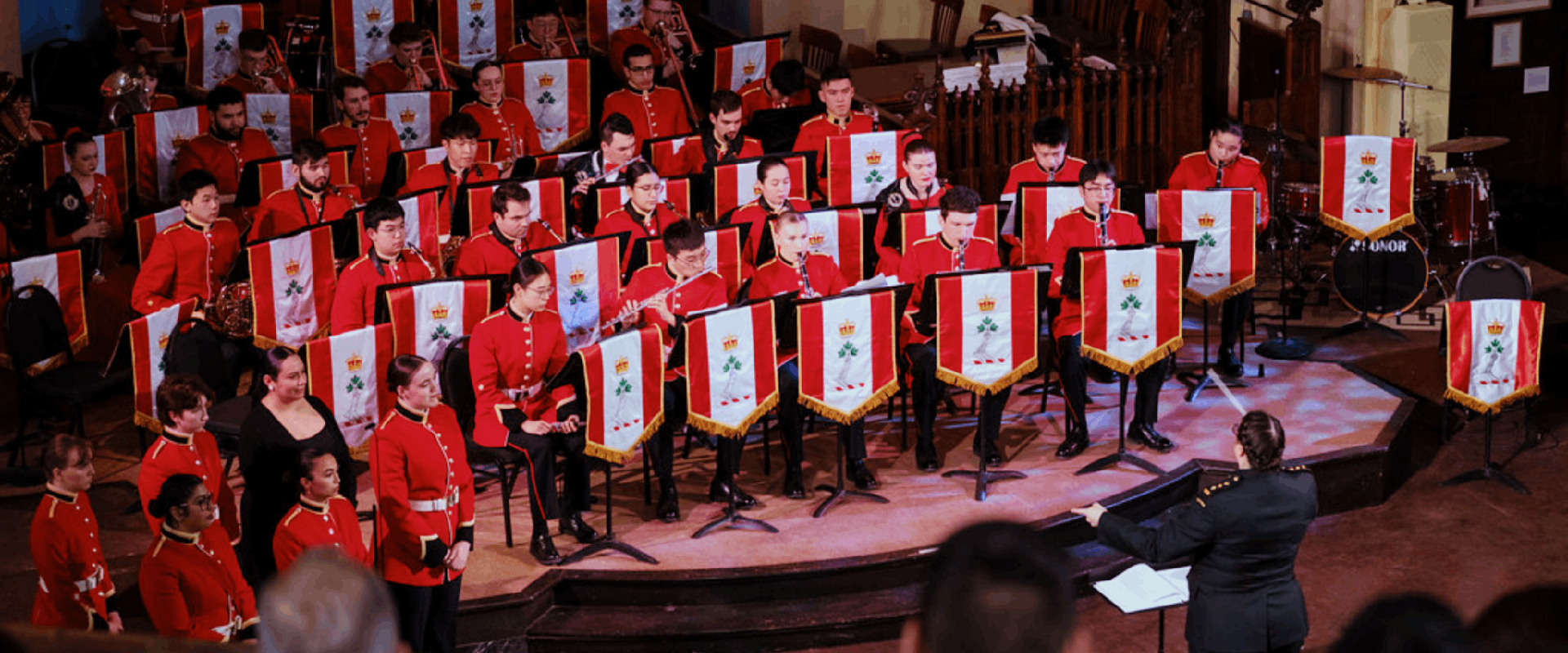 The Royal Military College Band performing on a stage in red uniforms.