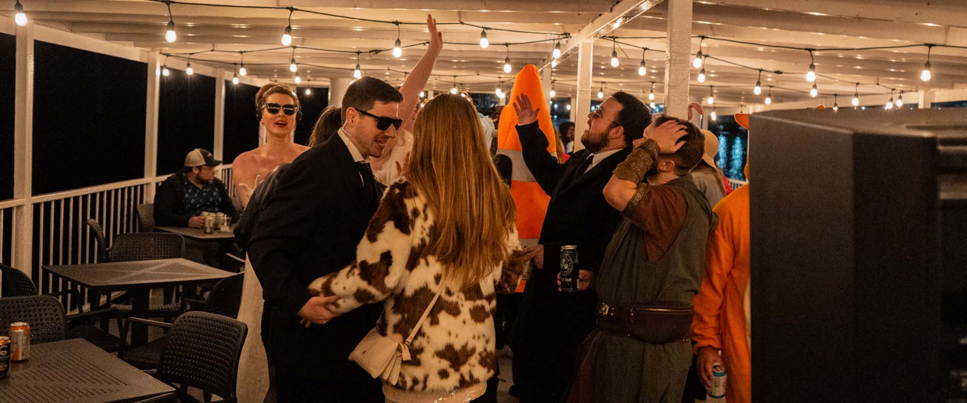 People in various halloween costumes dancing on a boat at night.