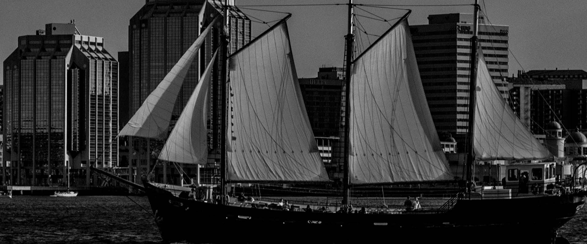 Tall Ship Silva in black and white sailing on the Halifax Harbour with the city of Halifax as the backdrop.