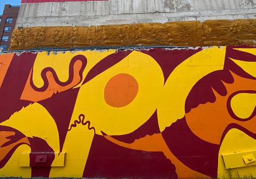 Mural on Grafton Street, titled "Mikisew" by Ininew and Anishinaabe artist Peatr Thomas. Abstract lines, an eagle, and Ininew syllabics are depicted in the mural in red, orange, and yellow colours.