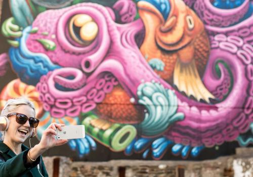 Woman taking a selfie in front of a Freak Lunchbox mural