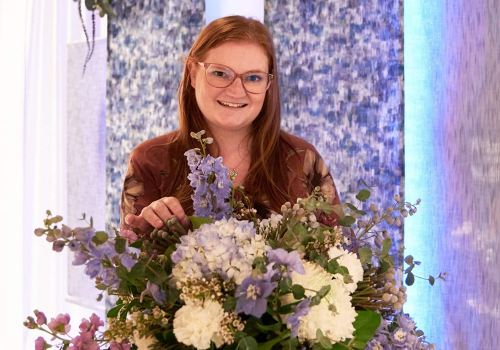 Meet Ashley Groves, owner of Happily Hitched Halifax, posing with a bouquet of purple and white flowers