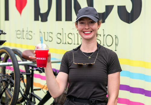 Person holding a red slushie in front of I Heart Bikes