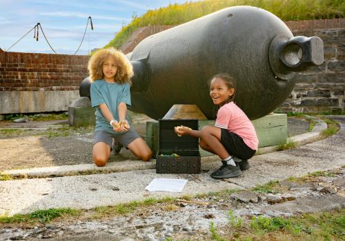 Two young boys with treasure chest in front of a cannon.