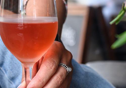 Person holding the stem of a glass of rose.