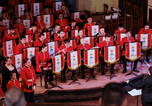 The Royal Military College Band performing on a stage in red uniforms.